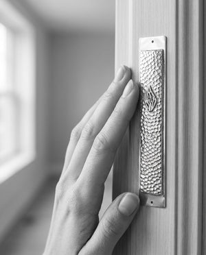 Hand gently touching a hammered silver Aesh Sheli mezuzah, traditional gesture, Kameart