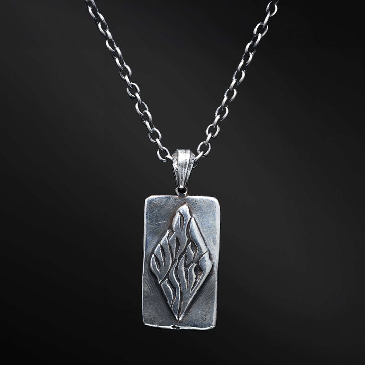 "Elkana Pendant: Unleash the power of your inner flame with the captivating Elkana pendant. Its elegant design showcases the phrase 'Aesh Sheli' engraved on a sleek plaque, representing the fire that resides within. Let its presence serve as a constant reminder of your inner strength, passion, and resilience as you navigate life's journey."